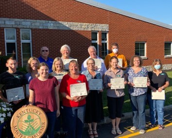 13 finishing participants of the 2022 Master Gardener Program hold their certificates and smile at the camera 